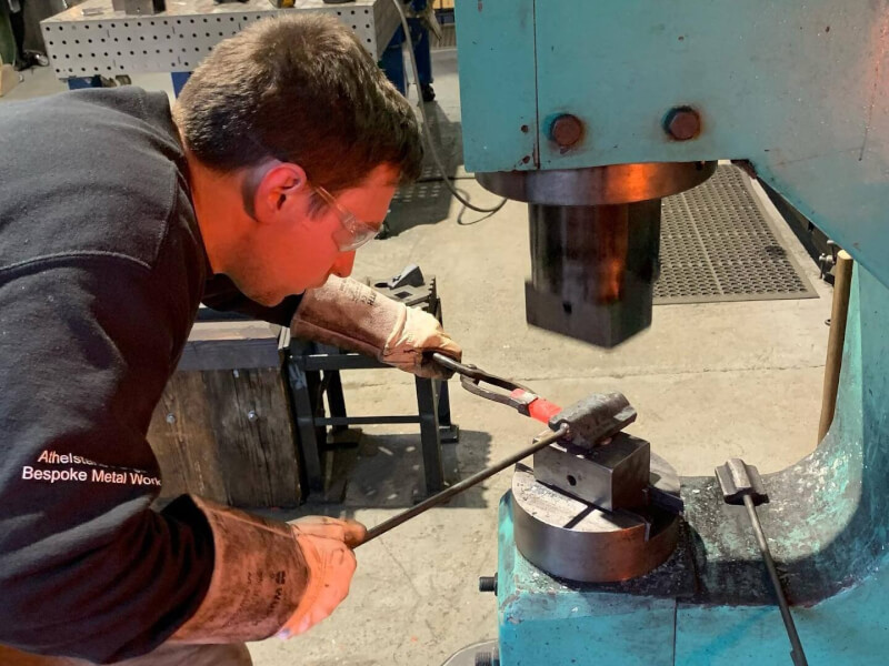 A man is using a tool to beat a piece of red hot metal into shape